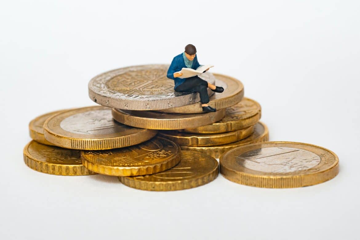 une miniature homme lisant un journal sur des pièces de monnaie